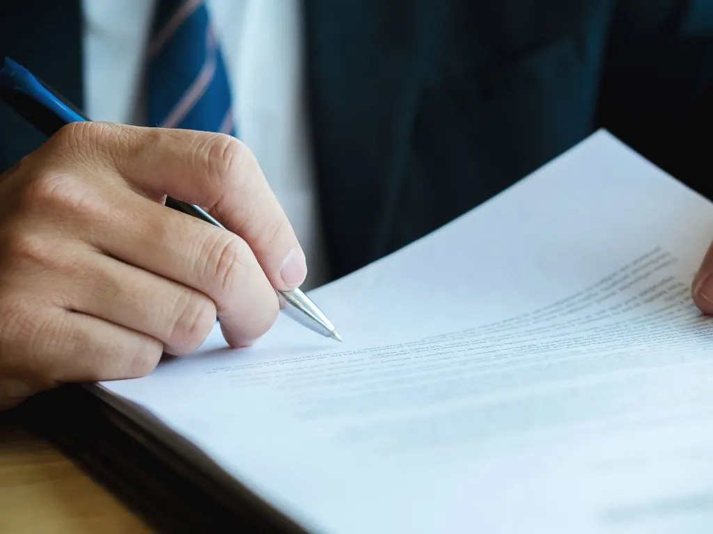 Mano di un uomo in giacca e cravatta che firma un documento con una penna