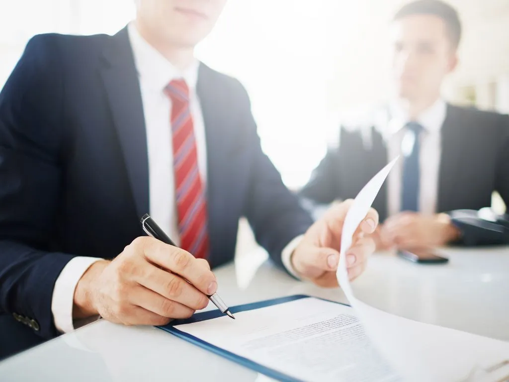Due professionisti in giacca e cravatta durante la firma di un documento a una scrivania
