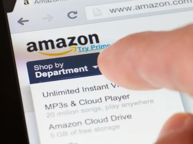 Schermo di uno smartphone con il sito di Amazon, mentre un dito tocca il menu Shop by Department